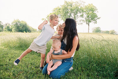 Mom sitting in a grassy field with her three children around her and in her lap