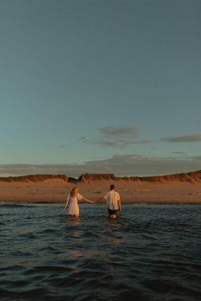 couple holding hands in ocean during lifestyle photos in pei