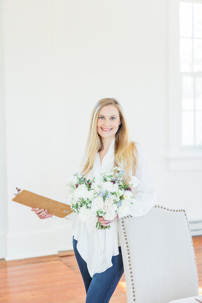 Washington DC Wedding Planner Kolena with Blue Sapphire Events poses with a bridal bouquet and a clipboard.