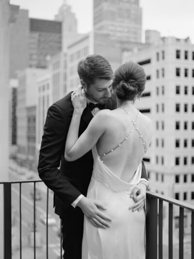 a groom embraces and kisses his bride, wearing a open back pearl back Jenny Yoo wedding dress on Shinola Hotel balcony in Detroit