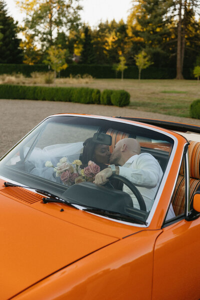 Wedding photos with bride and groom  kissing in an orange vintage car.