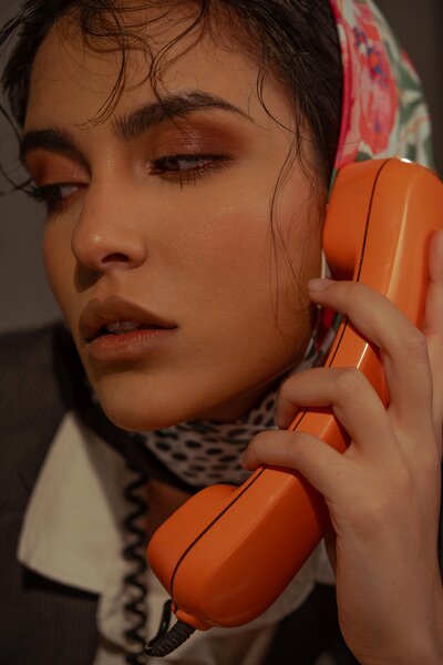 Up close of a woman holding an orange phone up to her ear.