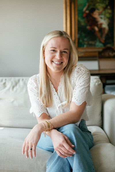 Headshot of a woman in a white top and jeans sitting on a couch