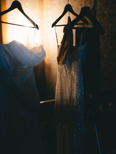 A series of sparkly sequined dresses hanging on clothing racks in a dimly lit room with dramatic lighting.