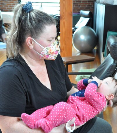 Katie wears a mask while holding a baby during a CST session.