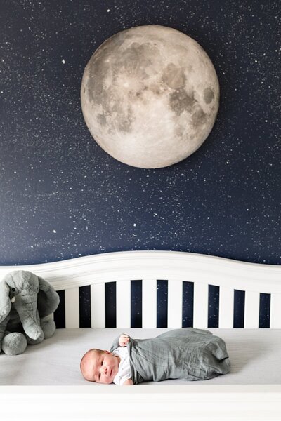 Newborn baby boy in crib with moon wall art in nursery