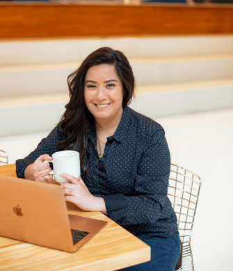 Mehroz Baig seated at a table with a coffee mug, smiling confidently in a relaxed work environment.