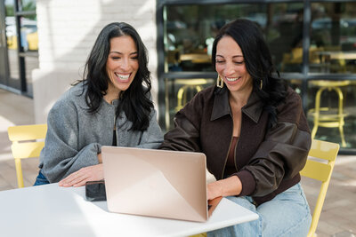 two women looking at laptop happily while sitting at cafe