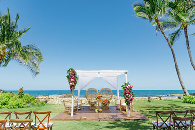 A wedding ceremony venue with two chairs under a small covering at the end of the aisle 