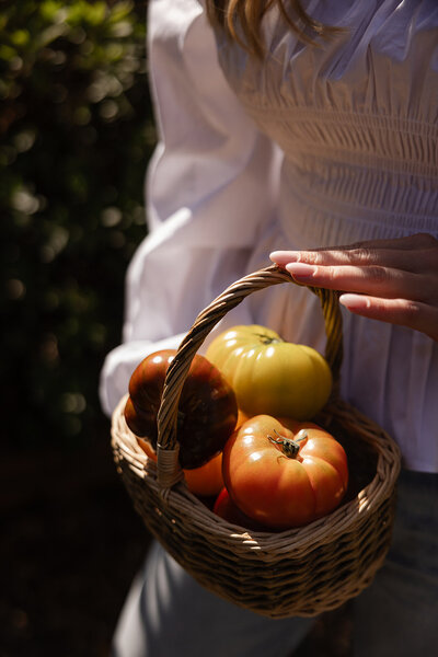 Functional nutritionist Tracy Greenstein holding a basket of tomatoes, representing seasonal whole foods