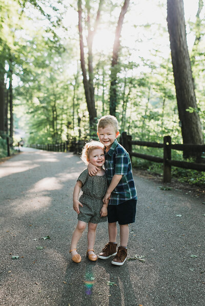 Family photoshoot with two young children hugging, outside on a walkway.