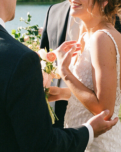 A man and woman exchange vows by a serene lake, surrounded by nature on their wedding day.