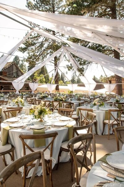 An elegant outdoor wedding setup with draped white fabric, wooden chairs, and floral centerpieces. Representing EventRent's vendor profile for the Crush Collective wedding show.
