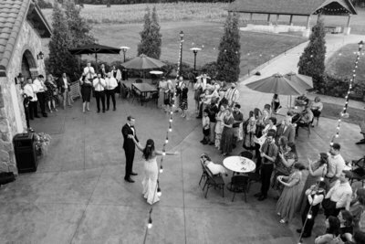 black and white photograph from overhead of bride and groom addressing wedding guests outside around tents lights and trees in minneapolis