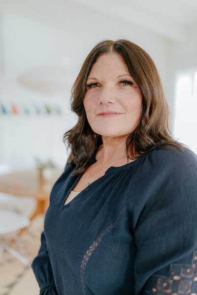Close-up portrait of Susie Schumacher wearing a navy blouse, standing in a bright modern space with soft natural light and a calm expression - Susie Schumacher Life Coach