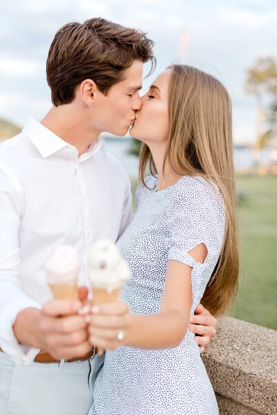 Engaged couple kiss while holding ice cream cone s in Stillwater Minnesota.