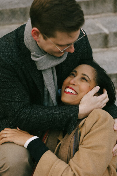 Couple snuggled up sitting on steps o keep each other warm in Boston, Massachusetts on a cold winter day, captured by Andrea-Marie Photography