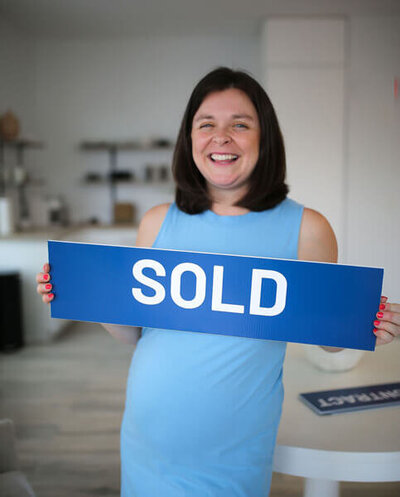 Ann-Marie Sepe holding a blue real estate yard sign that says “SOLD”