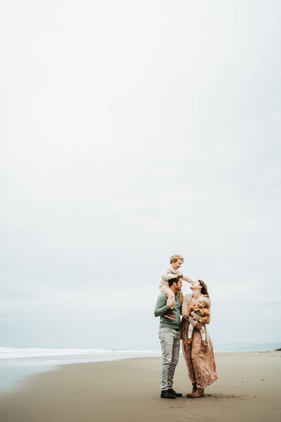 Pregnant mom holding her daughter and dad is giving mom hug