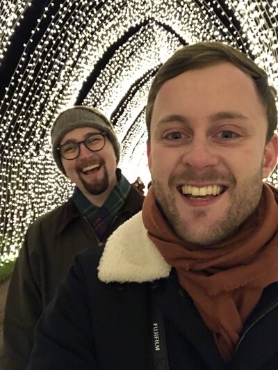 Aberdeen wedding photographer Scott takes a selfie with his husband under a large fairy light archway.