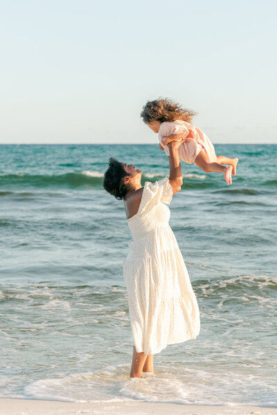 mother throwing young daughter into the air over the beach waves