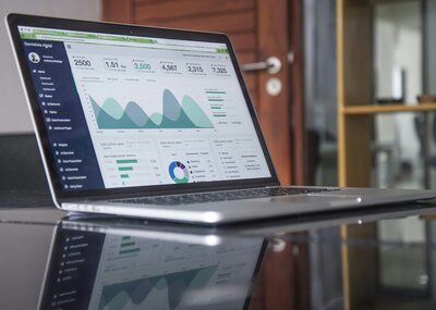 Laptop displaying a detailed business dashboard with charts, graphs, and user data analytics on a reflective black table in a modern office setting at Kidwell Coaching