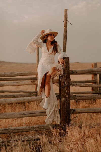 A bride sitting on the fence wearing a hat.