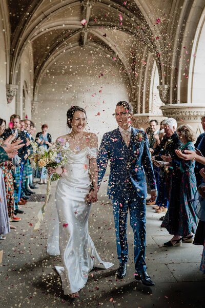 A portrait photograph of a bride and groom walking through confetti.