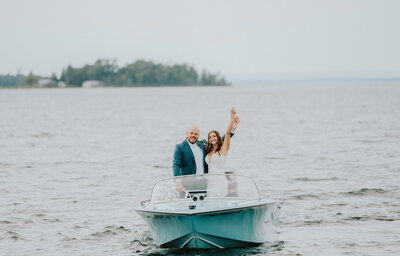 A bride and groom on a blue boat cheering to their Michigan wedding photographer in Grand Rapids