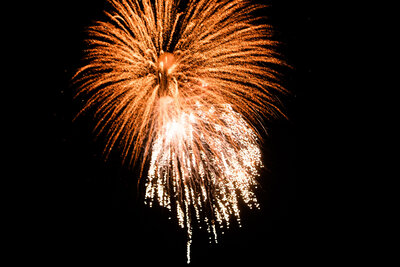 An orange and gold firework lights up the night sky, bursting in intricate patterns during a wedding celebration.