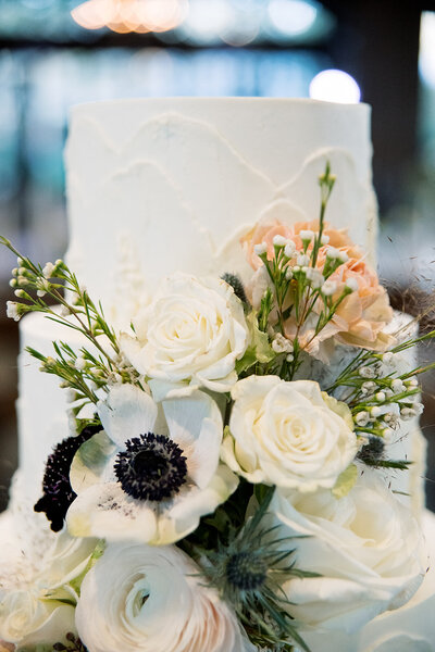 white tiered cake with white flowers and greenery on the cake