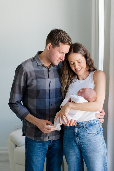 New parents stand next to baby's crib while she sleeps while holding her tight