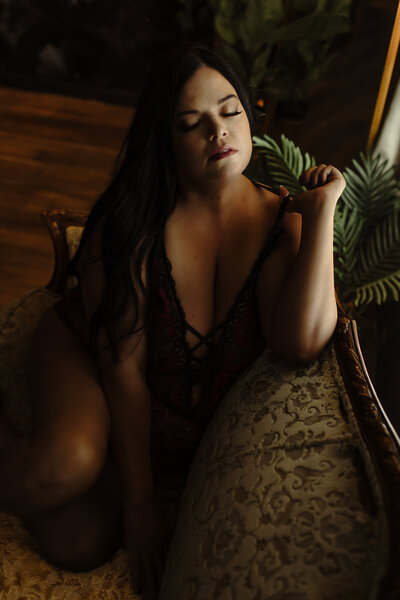Classic beauty in a boudoir setting: Dark-haired woman in black lace seated on a richly textured vintage couch.