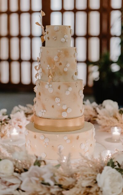 Tall tiered wedding cake with white and gold floral and pearl decorations; gold wafer paper ginko leaves