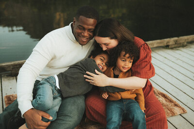 A toddler in a flowing blue dress takes confident steps through a sunlit field, as her smiling parents sit close behind, watching with love. This warm, golden-hour moment reflects the natural and candid style of a Portland family photographer