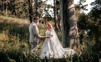 Bride and groom holding hands among tall green trees during their romantic forest wedding photoshoot in Auckland, captured by Zanthe Vorsatz Photography.