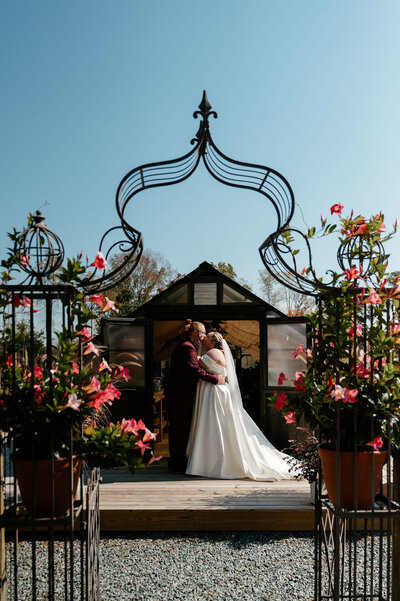 Couple kissing under floral arch in front of greenhouse