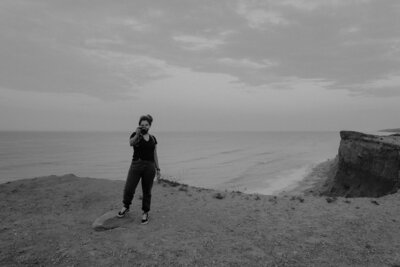 woman standing on cliff holding out camera