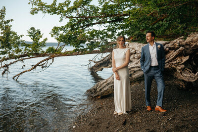 Bride and groom standing on a quiet lakeshore beneath low-hanging trees, captured by a Washington elopement photographer.