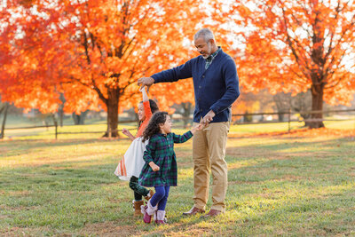 A dad dancing with his two little girls at a park in Northern Virginia at sunset.