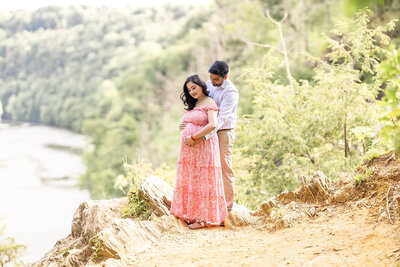 A father stands behind an expecting mother as he gently holds her belly and they both look at her belly with joy, photographed by Milford CT Photographer, Tambella Photography