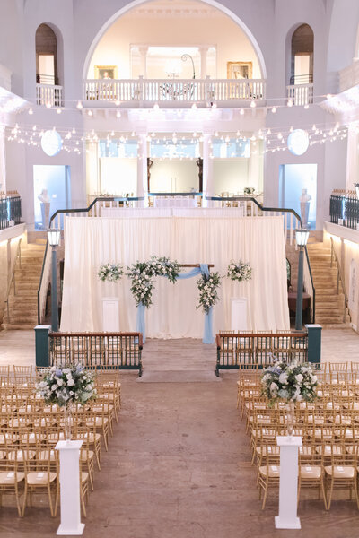 An empty wedding venue prepared with green and white flowers, twinkling lights, and seating