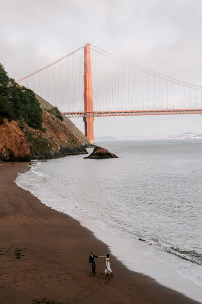 newlyweds dancing on beach in front of golden gate bridge