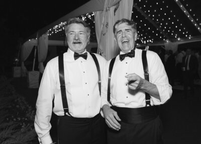 Black and white image of bride and groom holding hands and smiling walking into their wedding reception