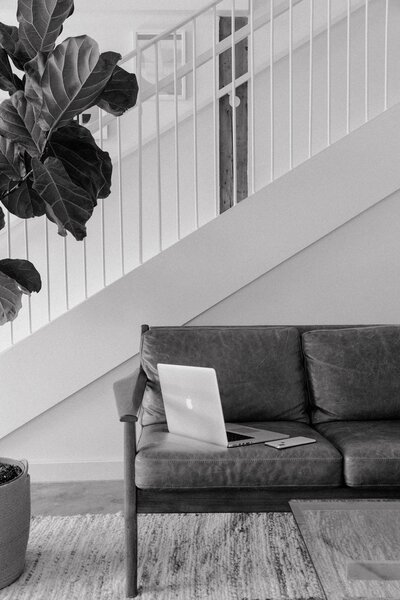 A laptop sits open on a gray leather sofa, likely displaying The White Label Way course content as a designer studies how to build their white label design business. The sleek workspace setup shows a comfortable learning environment for brand and web designers improving their skills and growing their businesses.