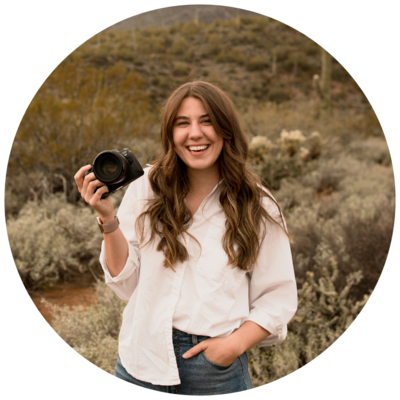 Photo of a woman photographer holding a canon camera and smiling at the camera