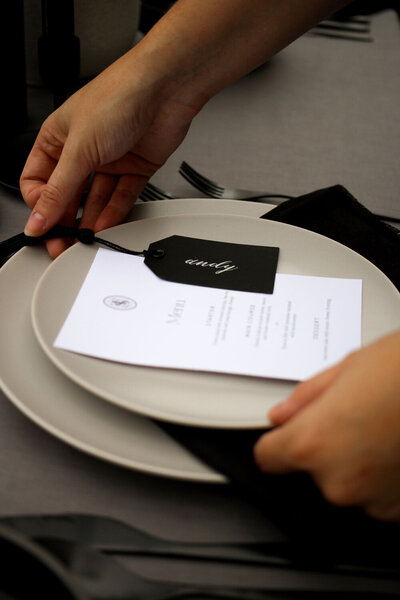 Hands placing a black name place card and white menu on a plate