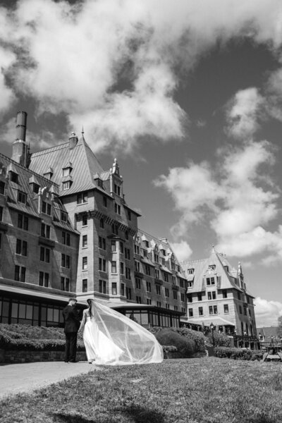 Le voile de la mariée s’élève dans le vent devant un majestueux manoir au Québec, créant une scène aérienne et spectaculaire d’un mariage élégant au charme intemporel