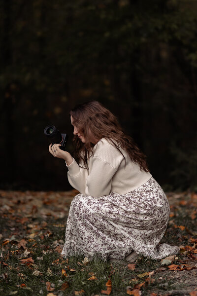 Girl crouched down in a fall dress holding a camera for her portraits of her side profile.