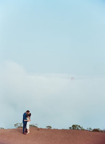 Wide view of a couple kissing after an exquisite mountaintop wedding with sky blue sky in the backdrop.